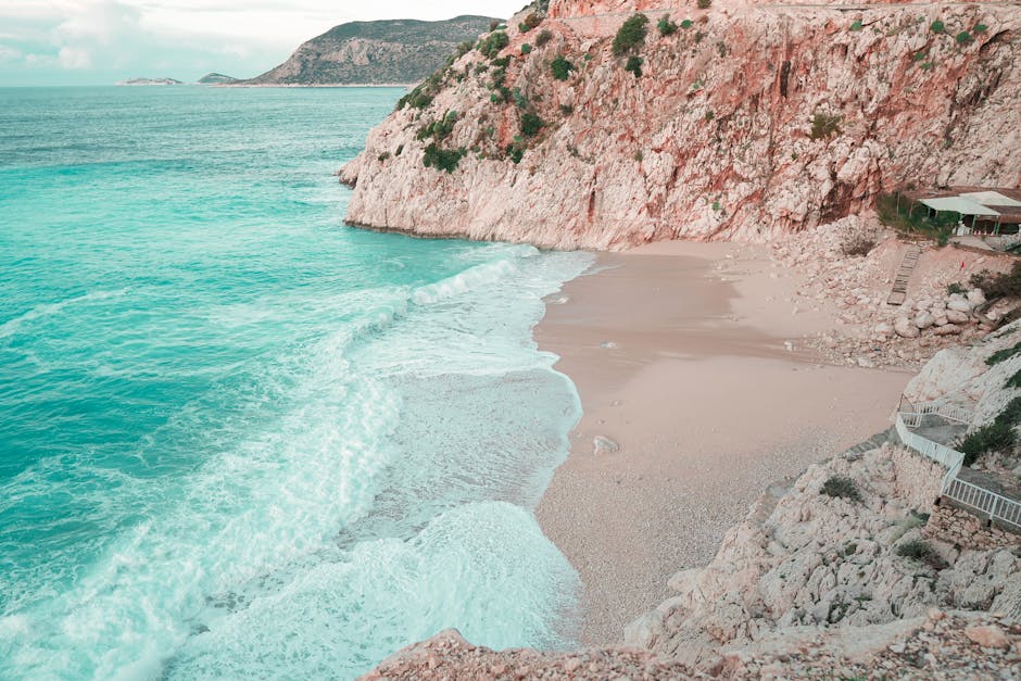 Serene view of sandy beach with waves crashing against rocky cliffs in Antalya, Türkiye